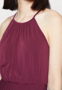 Körsbärsfärgade halterneckklänning med en insamlad bodice och elastisk midja, tillverkad av ett mjukt, lätt tyg. Utsmyckad med subtila veck.