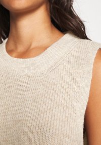 Hellbeiges ärmelloses Stricktop mit weitem Rundhalsausschnitt und strukturiertem Muster. Weicher Stoff mit leicht lockerer Passform.