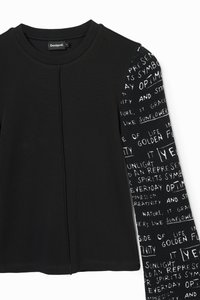 Black long-sleeve top with a textured black and white patterned sleeve featuring handwritten text. Ribbed fabric and crew neckline.