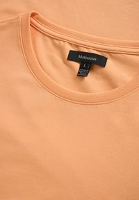 Peach-colored cotton t-shirt with a round neckline and short sleeves, featuring a black label with "Matinique" and size L. Texture is smooth.