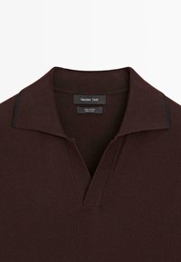 Burgundy bomullspolo med v-ringning, med en subtil texturerad yta och kontrasterande marina detaljer på kragen.
