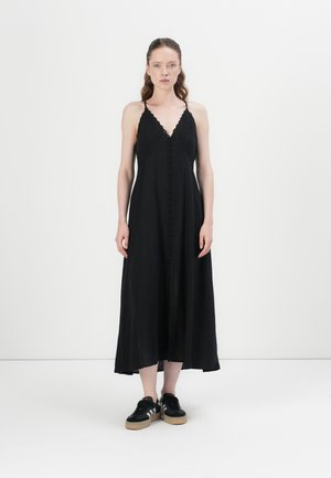Svart maxi-kjole med V-hals, blonde detaljer og knappefront. Båret med svarte sneakers med teksturert såle og striper.