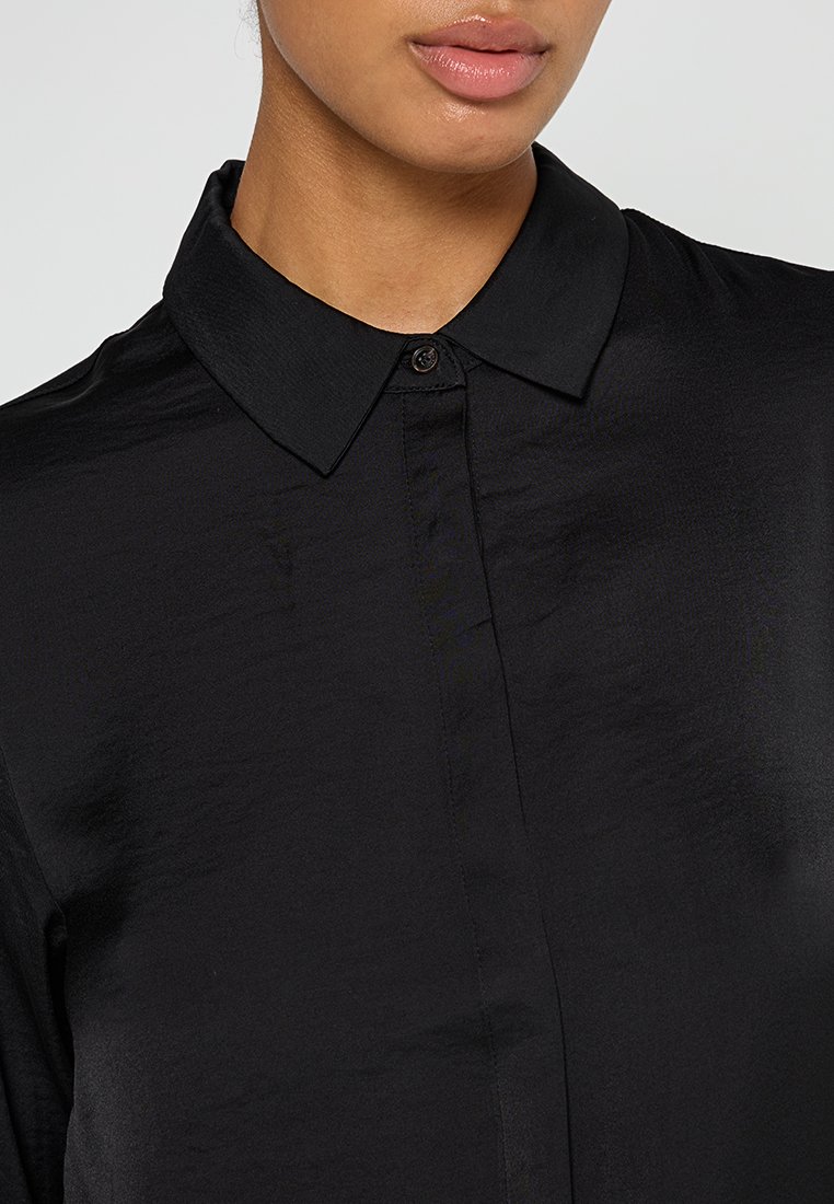 Zwarte shirt met een button-down kraag, een soepele textuur en een subtiele glans. Voorzien van een knoopsluiting aan de voorkant en een getailleerde pasvorm.
