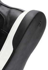 Zapatilla negra con parte superior de cuero y malla, suela de goma blanca y forro interior texturizado. Presenta un logo sutil en el talón y rayas finas en la suela.