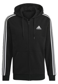 Sweat à capuche zippé noir en tissu doux, avec une poche kangourou, une capuche à cordon, et trois bandes blanches le long des manches. Logo Adidas visible.