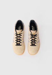 Baskets en suède beige avec lacets noirs, accents de motifs léopard sur les côtés et un logo doré sur la languette. Semelle en caoutchouc pour une bonne adhérence.
