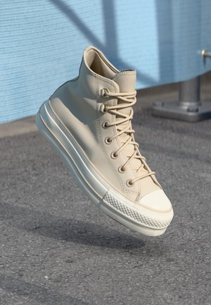 Sneaker high-top beige in pelle con superfice testurizzata, punta rotonda e suola in gomma bianca. Presenta un design con lacci e occhielli dorati.