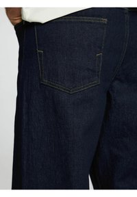 Temno modri jeans iz denima z oblikovanim krojem, ki imajo zadnji žep s kontrastnim rumenim šivom in gladko, teksturirano površino.