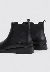 Black leather ankle boots with elastic side panels, rounded toe, and a low block heel. Features a small logo near the heel.