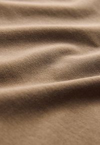 Helepruun kangas pehme tekstuuri ja õrna venivusega, millel on peen kudumismuster ning õrnad kortsud kogu pinnal.