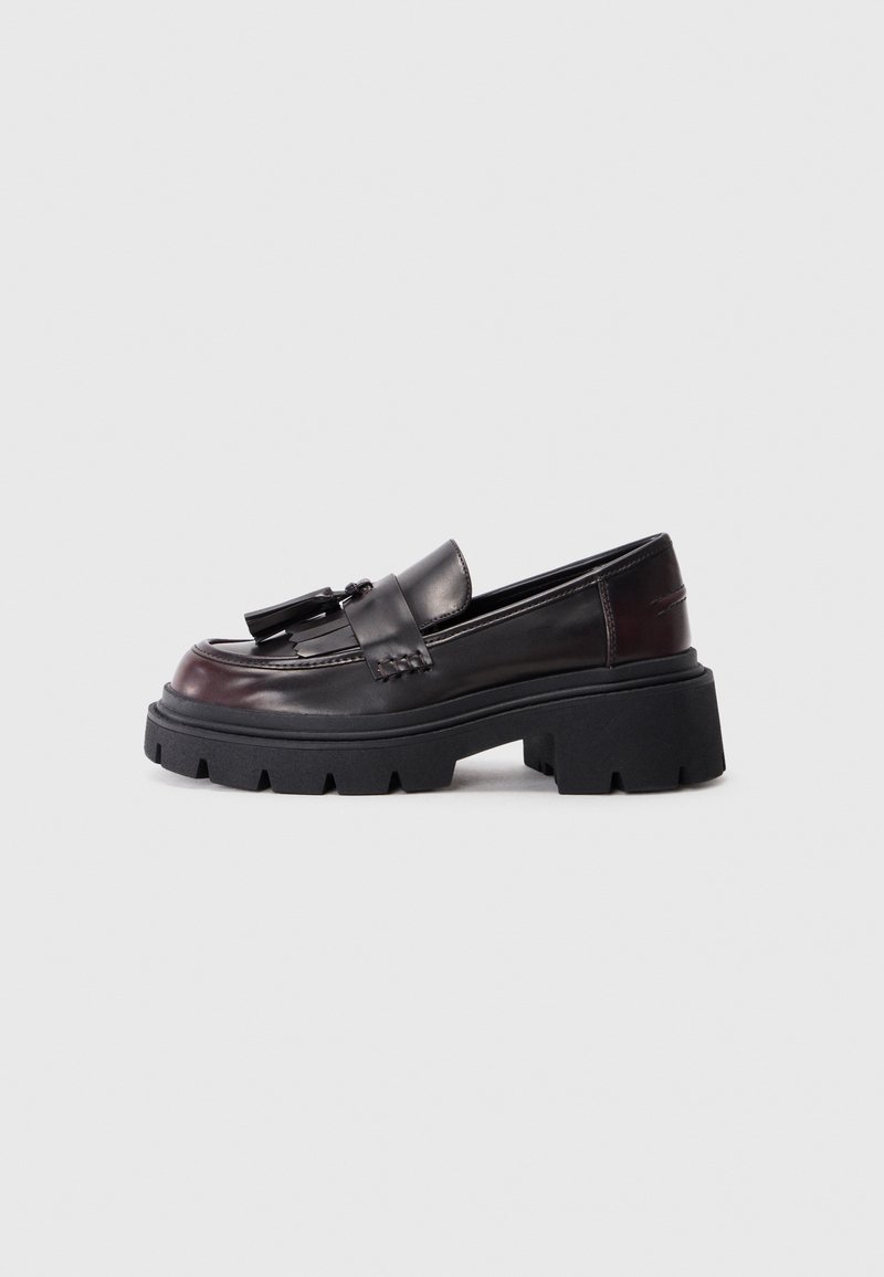 Loafers negri masivi din piele netedă, cu un accent împletit și o talpă plată din cauciuc cu un model pronunțat de profil.