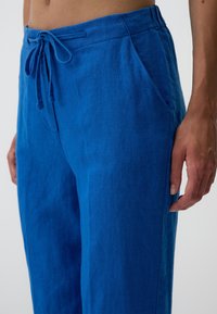 Blauwe linnen broek met een verstelbare tailleband, twee zijzakken en een relaxte pasvorm. De stof heeft een lichte textuur.