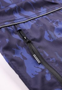 Μαύρο φερμουάρ με γλωσσίδα σε ύφασμα με μοτίβο παραλλαγής σε μπλε και μαύρο, με εμφανείς λεπτομέρειες ραφής.