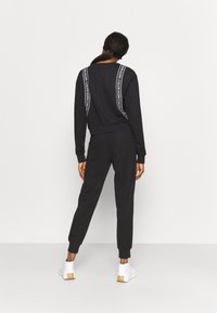 Ensemble sweat-shirt noir et joggers avec accents de logo blancs. Tissu doux, coupe décontractée et poignets côtelés. Baskets blanches complètent le look.