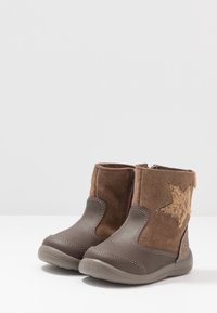 Hnědé kotníkové boty s semišovým svrškem, šedou syntetickou špičkou a akcentem hvězdy. Texturovaný povrch s hladkou gumovou podrážkou.