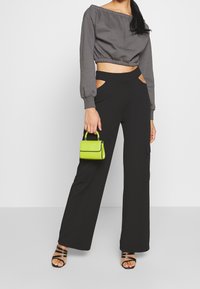 Suéter gris recortado con cinturilla elástica, pantalones cargo negros de talle alto y un pequeño bolso verde. Sandalias negras con tiras completan el look.