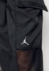 Zwarte sportshorts met mesh-accenten, voorzien van een met rits sluitende zak en een wit geborduurd logo. Gemaakt van lichtgewicht, gladde stof.