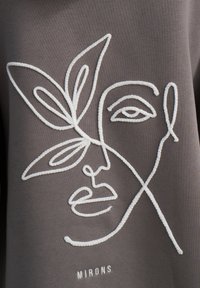 Tessuto grigio con ricami bianchi che raffigurano il disegno di un volto e una foglia. Il testo "MIRONS" è ricamato sotto il design. Texture liscia, stile minimalistico.