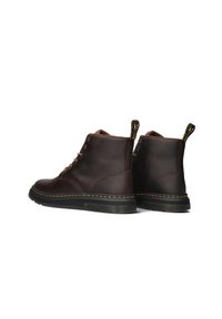 Brown leather ankle boots featuring a round toe, gold eyelets, a contrasting yellow stitching detail, and a patterned pull tab at the heel.