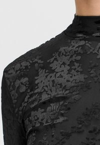 Maglietta nera a maniche lunghe con un motivo floreale testurizzato, tessuto liscio con un leggero lucido, scollatura alta e design aderente.