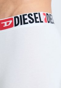 Bijela pamučna donja rublja s kontrastnim crnim i crvenim elastičnim pojasom na kojem je u podebljanim slovima ispisan logo "DIESEL".