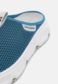 Μπλε δίχτυ σλάιντ παπούτσι με υφή στο επάνω μέρος, λευκή σόλα και μαύρη ετικέτα λογότυπου, διαθέτοντας στρογγυλή σιλουέτα και ελαφρύ σχεδιασμό.