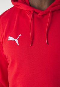 Red hoodie made of cotton blend fabric, featuring a white embroidered Puma logo on the left chest and adjustable drawstrings on the hood.