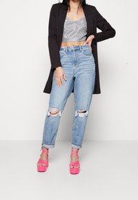 Svart lång kavaj över en silverfärgad kort topp, tillsammans med nötta ljusblå jeans och klarröda platåsandaler.