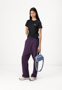 Svart t-skjorte med logo, løse lilla joggebukser og en liten denimhåndveske med blå stropp. Kraftige sneakers fullfører antrekket.