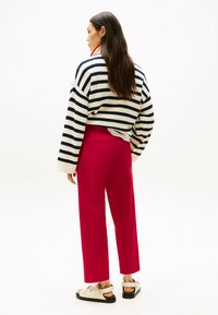 Pull en maille rayé bleu marine et blanc, associé à un pantalon taille haute rouge sur mesure et des sandales beiges. Texture lisse, coupe décontractée.