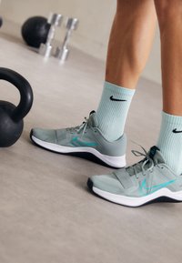 Las zapatillas deportivas de color gris claro presentan un diseño de malla transpirable con acentos en turquesa. Se usan con calcetines de menta acanalados, junto a una kettlebell y mancuernas.