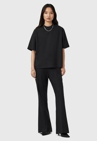 Zwarte oversized T-shirt met korte mouwen gecombineerd met zwarte, high-waisted, flared broeken. Het materiaal lijkt soepel; zilveren kettinghalsband accentueert.
