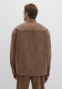 Braunes Kordhemd mit lässiger Passform, das vertikale Streifen, einen spitzen Kragen und geknöpfte Manschetten aufweist. Glatte Textur, lässiges Design.