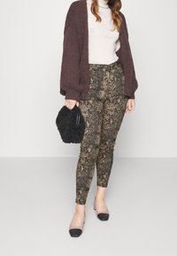 Brun stickad kofta, gräddvit polotröja, byxor i ormskinnsmönster i guld och svart, svart texturerad handväska, genomskinliga klackar med svarta spetsar.