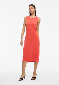 Vestido midi sin mangas en un vibrante color coral, confeccionado en una tela suave y ligera con silueta recta y aberturas laterales. Combinado con mule negras.
