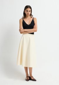 Zwarte mouwloze top met een diepe V-hals, gecombineerd met een vloeiende crèmekleurige midi-rok. Kenmerken zijn een gladde stoftextuur en een klassieke vorm.