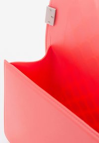 Koraalkleurige handtas met een gladde textuur en een metalen sluiting. Het interieur heeft een gestippelde voering en biedt een ruime compartiment.