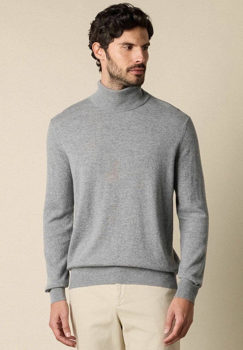 Maglione grigio a collo alto realizzato in morbido tessuto knit, caratterizzato da maniche lunghe e polsini e orlo a coste. Design minimalista con una texture liscia.