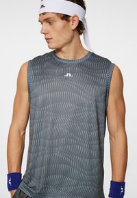 Canotta sportiva senza maniche di colore grigio scuro con motivi a onde bianchi. Presenta un colletto rotondo e include fasce per i polsi di colore blu.
