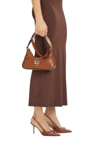 Bolso de cuero marrón con herrajes plateados y logo, sostenido por una persona con un vestido marrón, combinado con tacones altos marrones a juego.