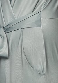 Vestido envolvente de satén en verde claro con cintura ajustable, bolsillos sin costura y textura suave con un brillo sutil. Costuras detalladas visibles.