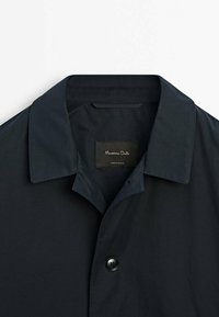 Tummansininen napitettavassa paidassa on leveä kaulus, se on sileäpintainen ja sisäpuolella on etiketti, jossa lukee "Massimo Dutti."