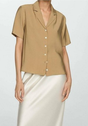 Chemise à manches courtes avec col, en tissu brun clair, coupe décontractée, dotée de boutons blancs sur le devant. Associée à une jupe en satin.