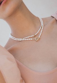 Dobbelt-strenget perlekæde udstyret med hvide perler, guldfarvede detaljer og en dekorativ lås med et unikt design.