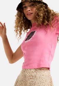 Pink cotton short-sleeve t-shirt with a black floral graphic and white text. Paired with a light brown skirt featuring a floral pattern.