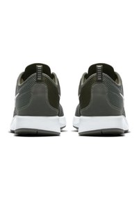 Mörkgröna sportskor med ett strukturerat mesh-överkänsla, vit mellansula och svart yttersula; har en dragflik vid hälen och en minimalistisk design.