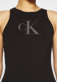 Czarny top bez rękawów wykonany z elastycznej tkaniny, zdobiony dużym, stylizowanym logo 'ck' oraz powtarzającym się wzorem tekstu w kolorze białym.