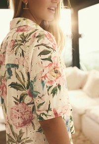 Blommönstrad skjorta i lätt tyg, med rosa och blå blommor på en krämfärgad bakgrund, med utskärningar och kort krage.