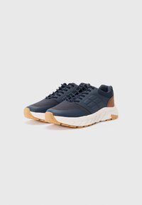 Navy blue sneakers with a textured fabric upper, white midsole, and gum rubber outsole. Features brown accents on the heel and side.