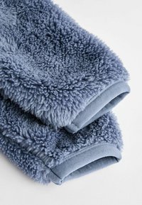 Modrý chlupatý textil, měkký fleece materiál s texturovaným povrchem. Má hladký modrý látkový lem na okrajích.